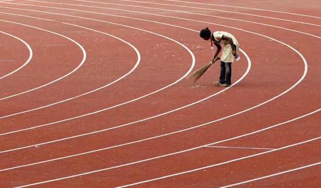 Una operaria tratando de limpiar la pista de atletismo de los Juegos de la Commonwealth con una simple escoba.