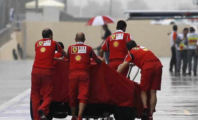 Ingenieros de Ferrari empujan un coche cubierto en la zona de boxes bajo la lluvia en el Circuito Yas Marina en Abu Dhabi