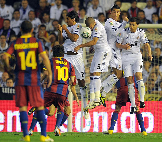 Los jugadores del Madrid saltan para tapar una falta botada por Messi.