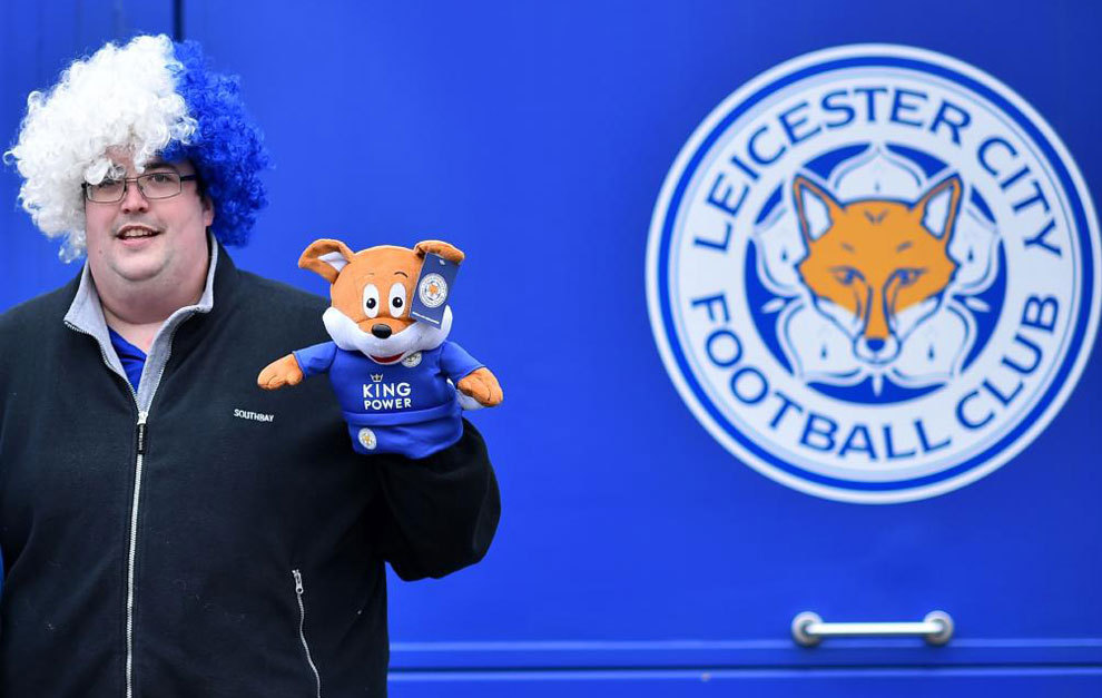 Un hincha del Leicester con la mascota del club y una peluca.