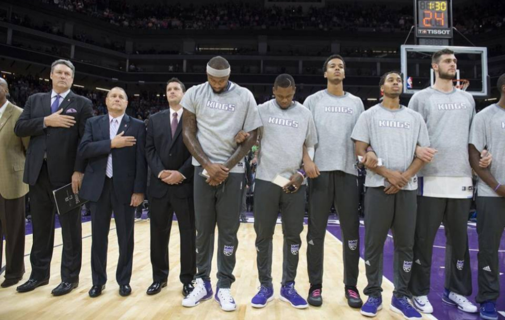 Jugadores de Sacramento Kings escuchan el himno nacional.