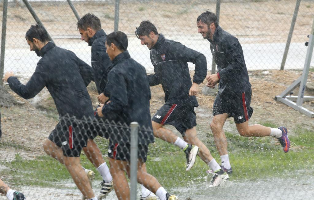 Los jugadores del Sevila corren para resguardarse de la lluvia en el...
