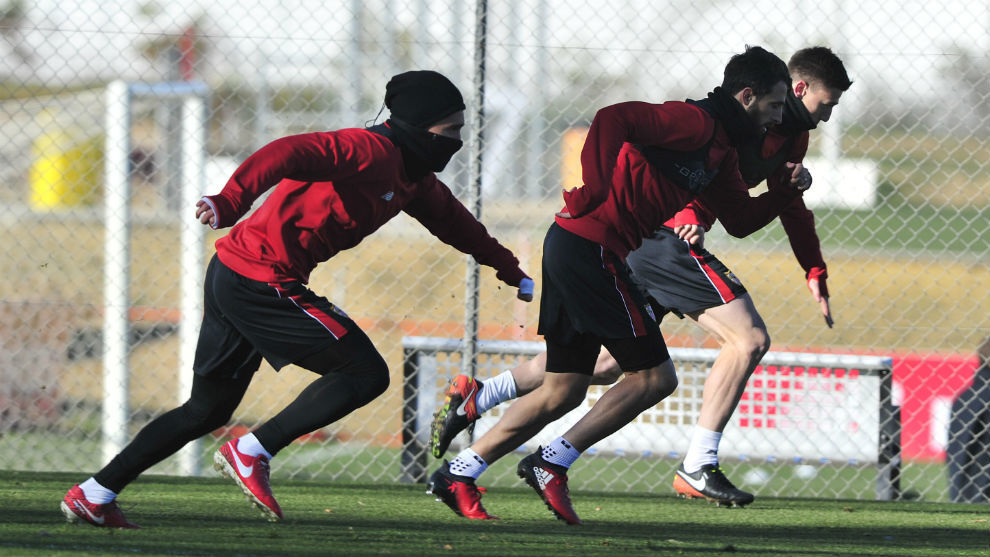 Tres jugadores del Sevilla, muy abrigados, hacen un sprint en el...