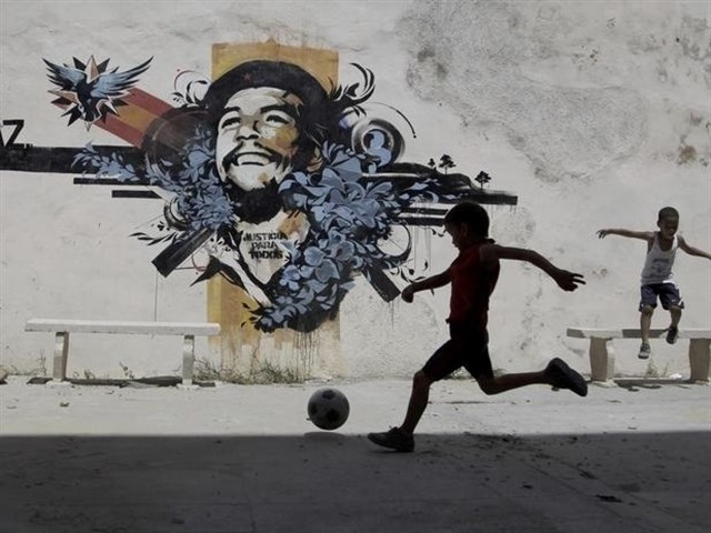 Un nio juega al ftbol en una plaza con un mural del Che Guevara.