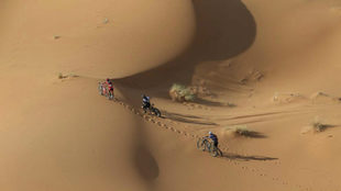Tres ciclista atravesando una de las grandes dunas del recorrido.