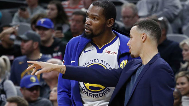 Stephen Curry charlando con Kevin Durant en un partido de los Warriors