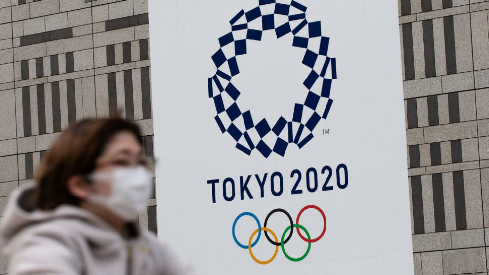 Una mujer pasea con mascarilla delante del logo de los Juegos de...