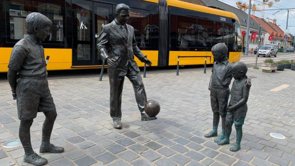 La estatua de Puskas dando toques a un balón junto a unos niños en la calle Bécsi.