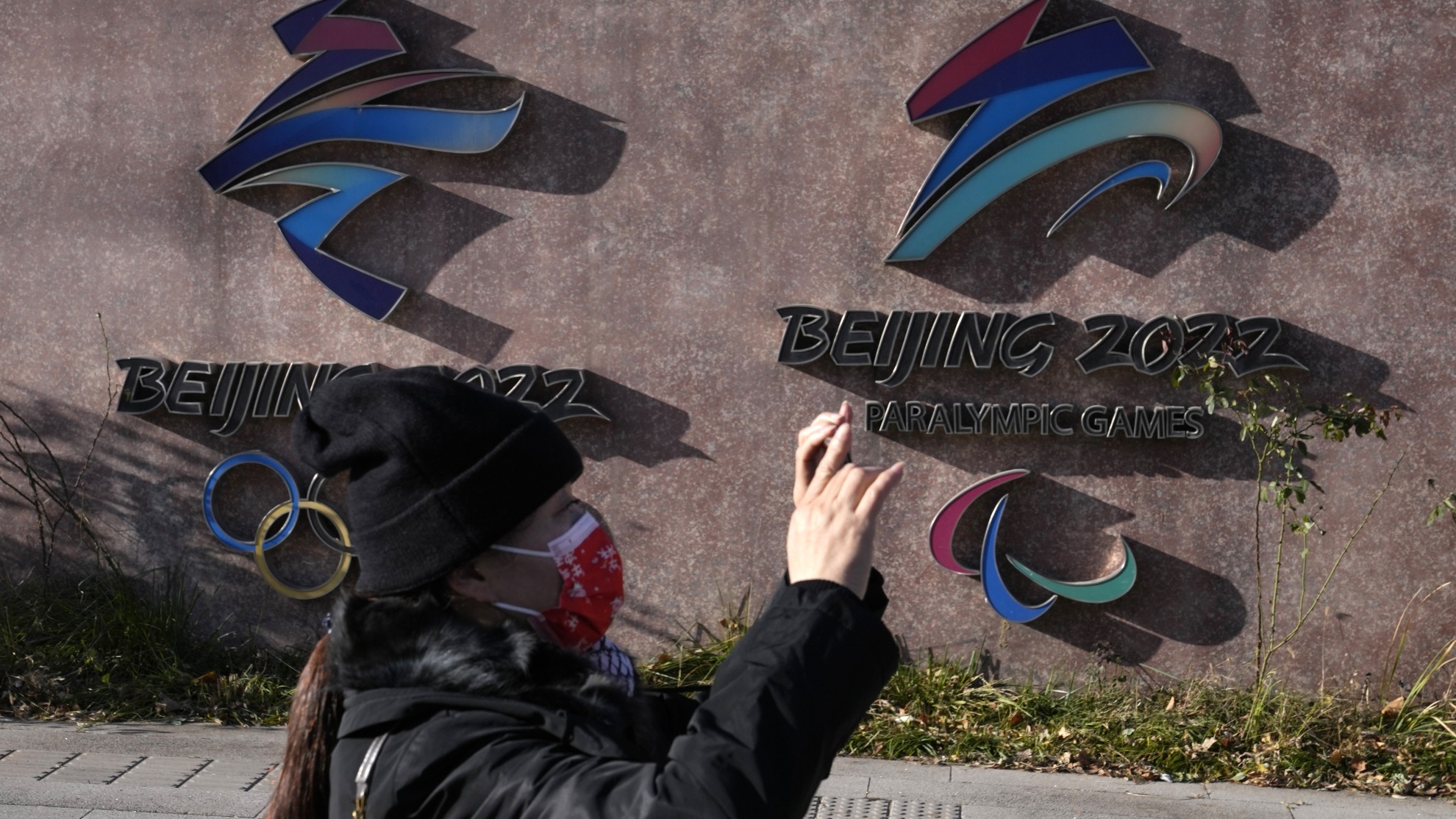 A woman wearing takes photos near the logos for the Beijing Winter Olympics and Paralympics in Beijing.