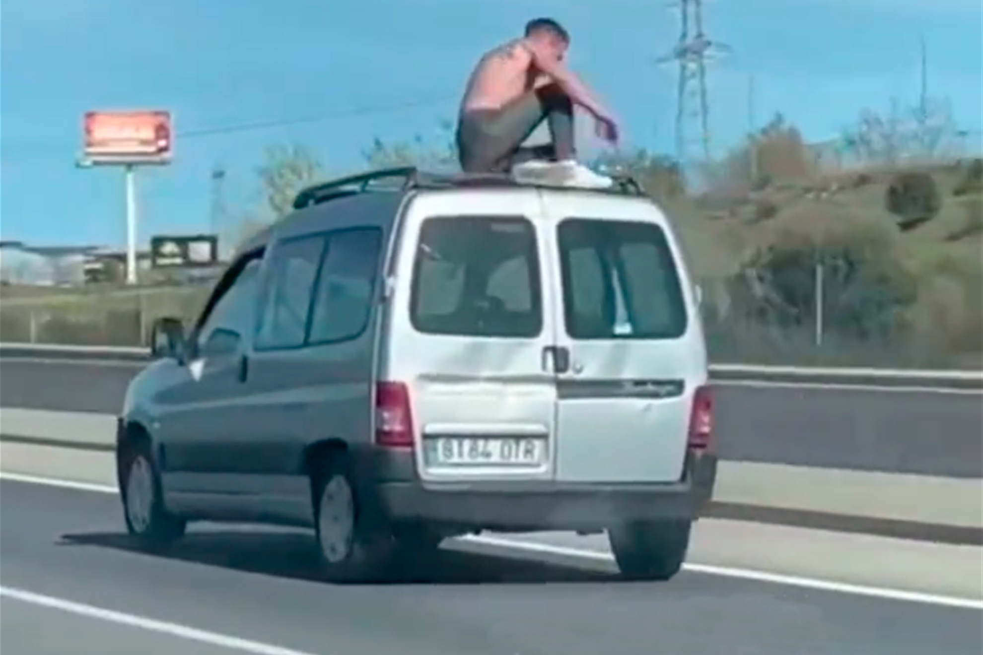 Un hombre, en el techo de un coche mientras este circula por una autovía.