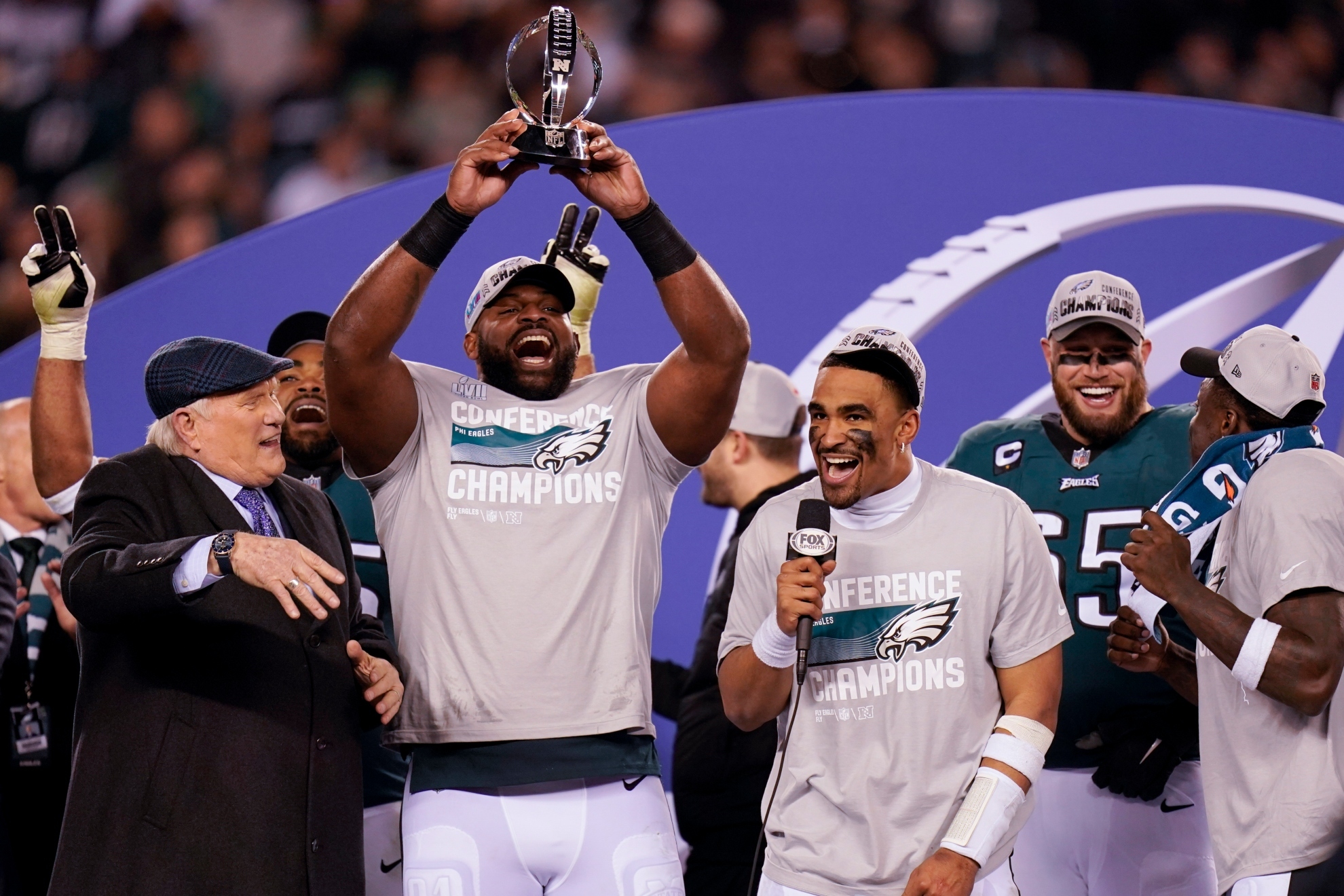 Terry Bradshaw, left, reacts as Philadelphia Eagles defensive tackle Fletcher Cox, second from left, hoists the George Halas Trophy as quarterback Jalen Hurts, center, holds a microphone after the NFC Championship NFL football game between the Philadelphia Eagles and the San Francisco 49ers