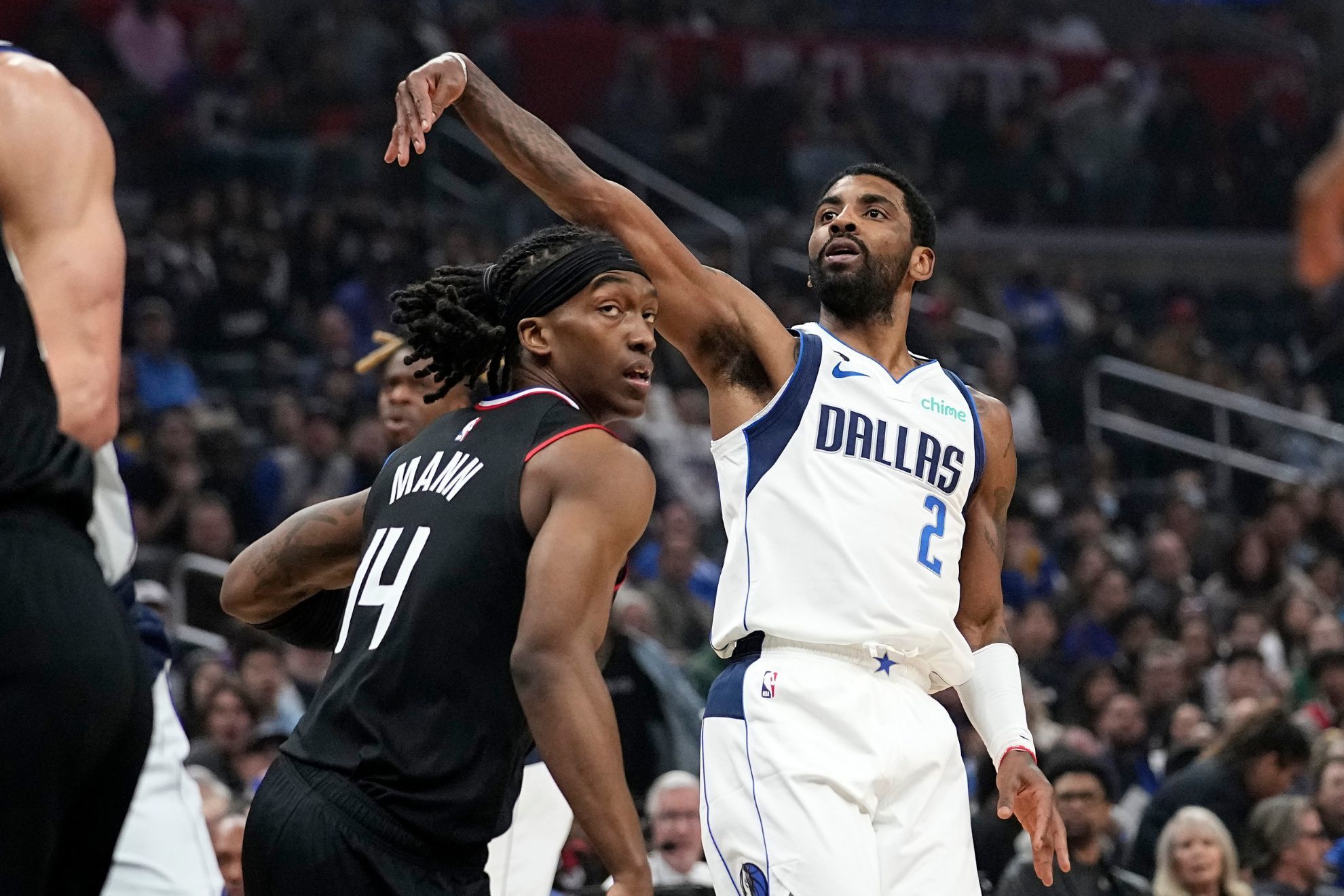 Dallas Mavericks guard Kyrie Irving, right, follows through after shooting as Los Angeles Clippers guard Terance Mann defends.