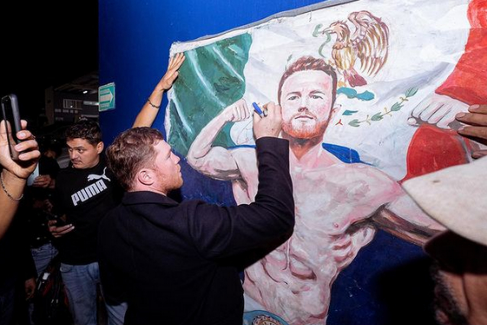 Saul "Canelo" Alvarez signs a portrait of him with a Mexican flag in the background.