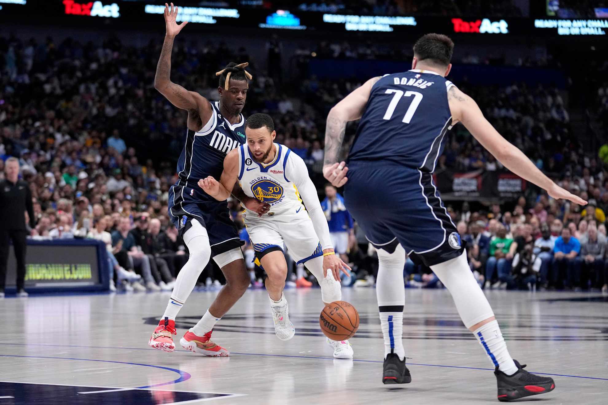 Golden State Warriors guard Stephen Curry (30) works to the basket as Dallas Mavericks forward Reggie Bullock, left, and Luka Doncic (77) defend in the first half of Warriors vs Mavericks.