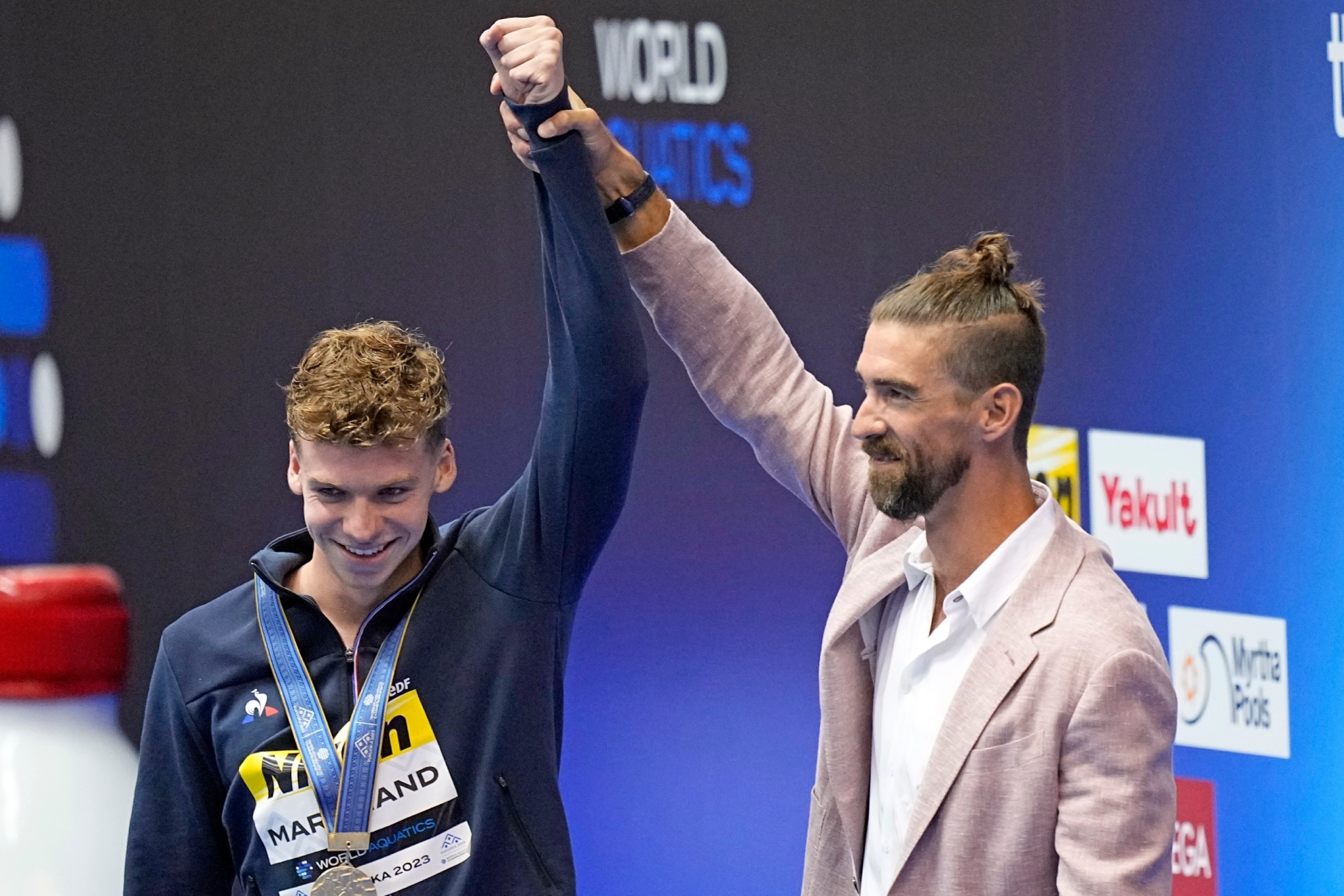 Michael Phelps levanta el brazo de Leon Marchand tras la ceremonia de medallas