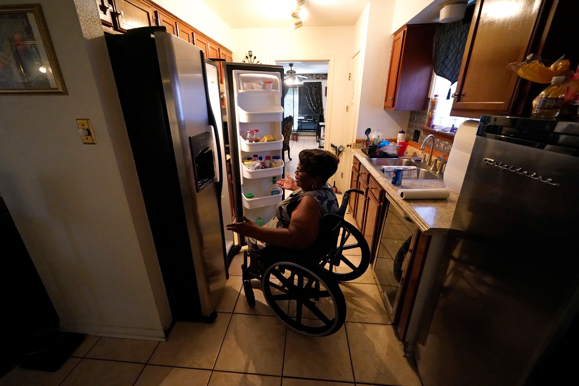 A woman looking for stuff on her fridge in a wheelchair.
