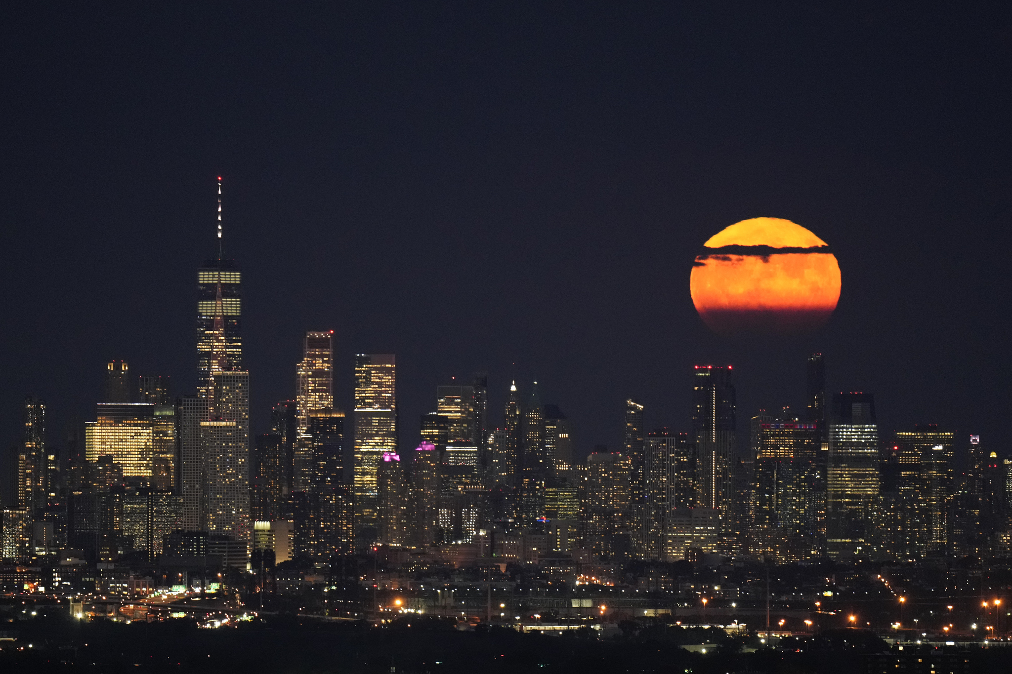 The moon rises through clouds over the skyline of lower Manhattan.