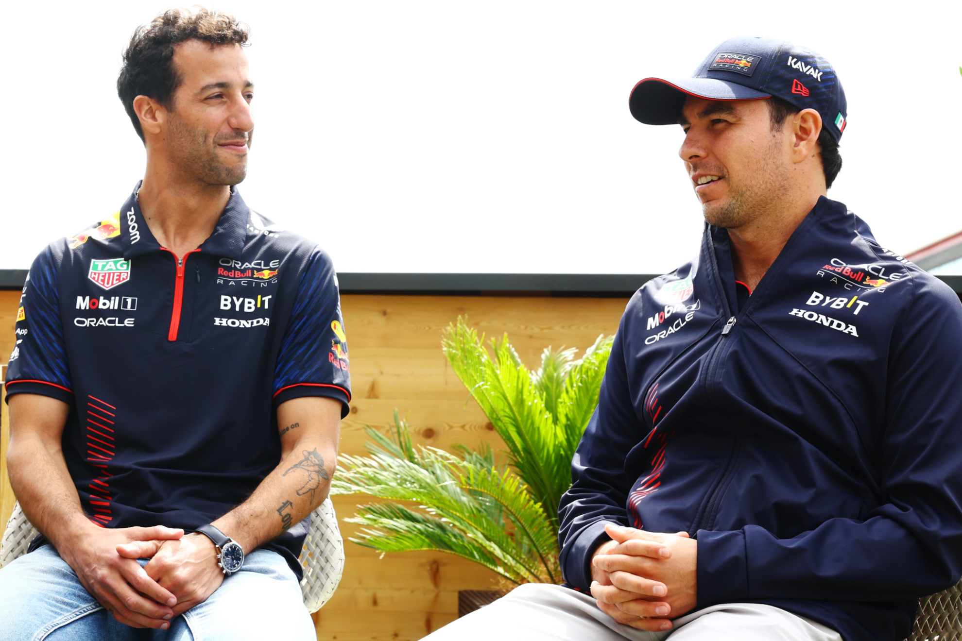 Daniel Ricciardo presta atención a un comentario de Checo Pérez.