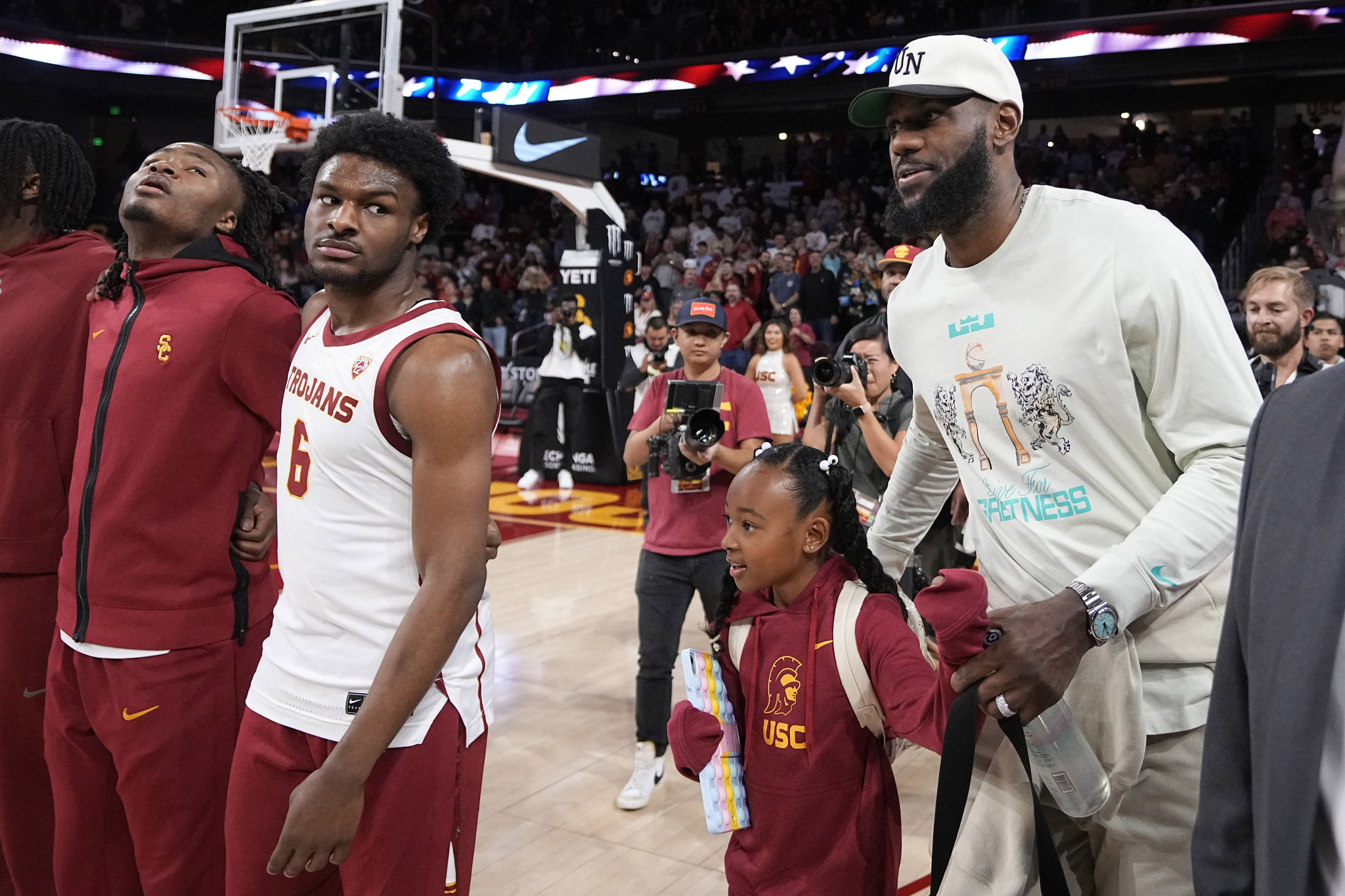 Southern California guard Bronny James stands on the court with the rest of his team as his father, LeBron James walks by prior to an NCAA college basketball game against Long Beach State Sunday, Dec. 10, 2023, in Los Angeles. (AP Photo/Mark J. Terrill)