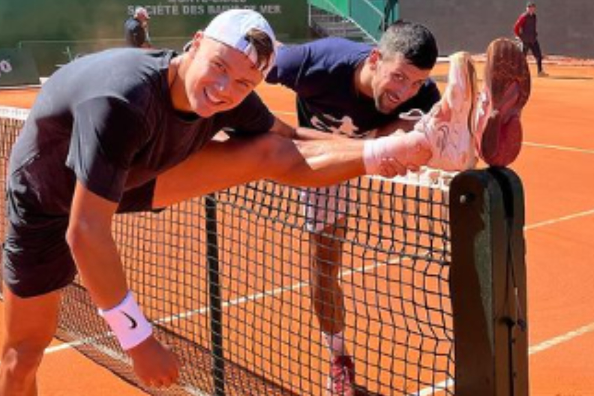 Rune y Djokovic estirando sobre la red de la central del Montecarlo Country Club